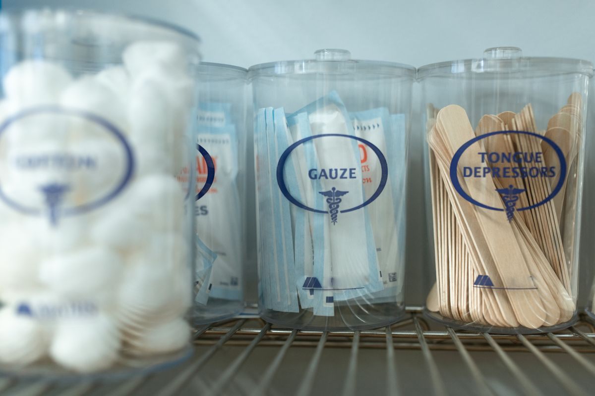 Clear clinic jars labeled cotton, gauze and tongue depressors on a wire shelf
