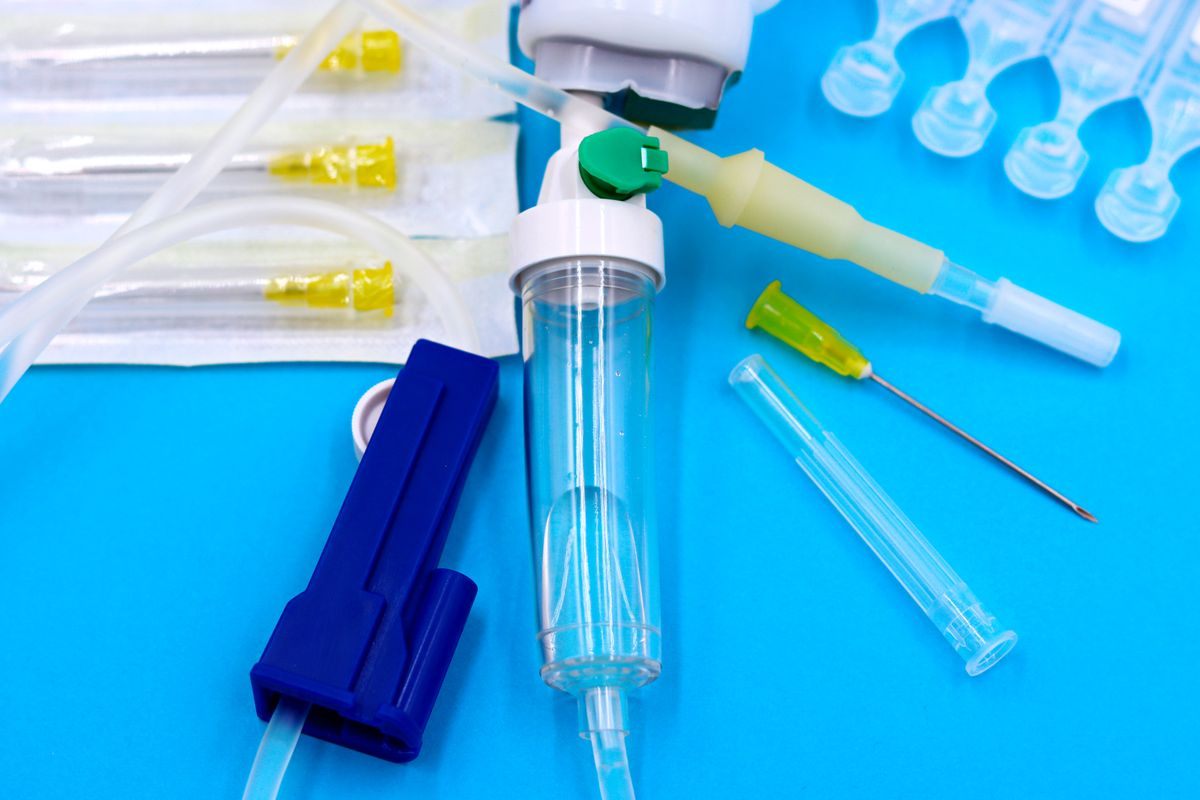 IV giving set with clear tubing, drip chamber and roller clamp beside needles on a blue background