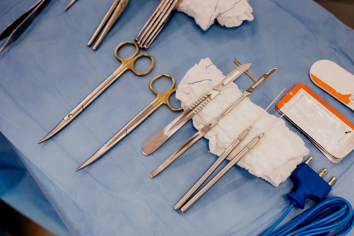 Surgical scissors, forceps and white gauze laid out on a blue surgical drape