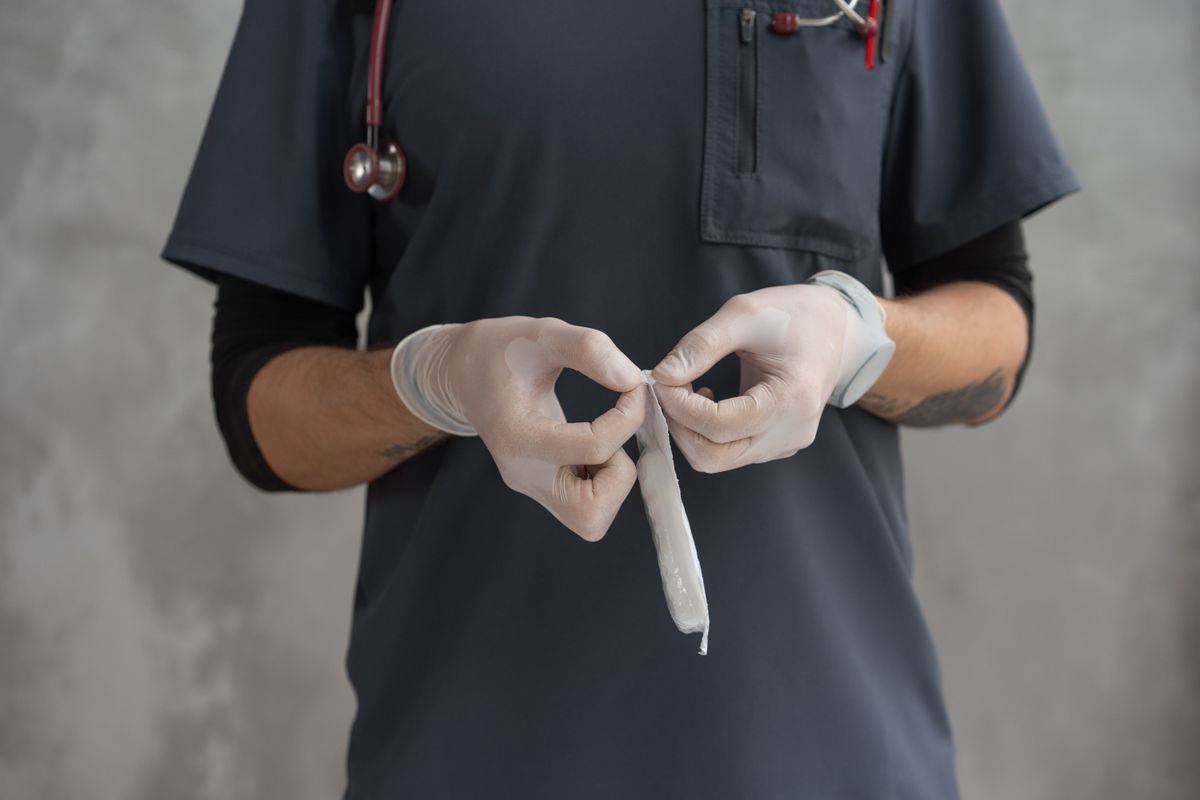 Gloved clinician in scrubs with a stethoscope holding a torn strip of roll gauze